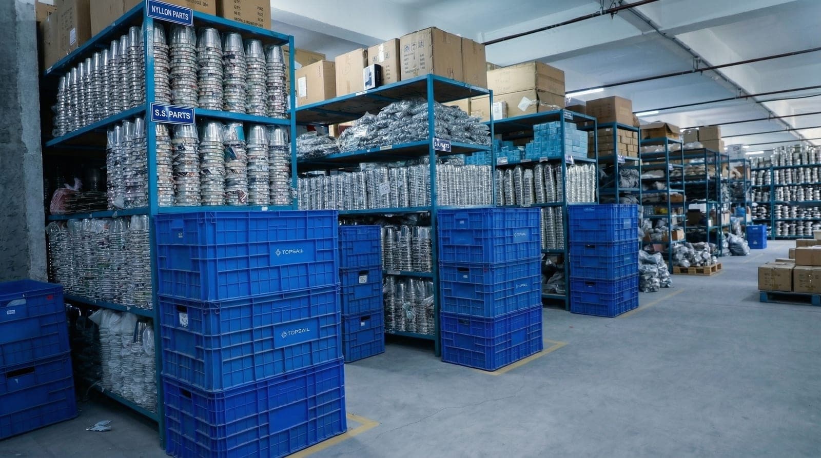 Stainless steel and nylon appliance components stacked in TOPSAIL crates at the Silvassa parts warehouse
